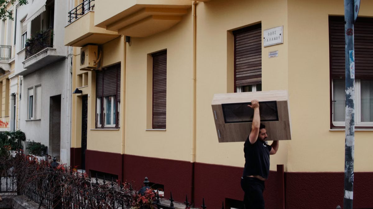 Photo of a man carrying a large box on a city street near colorful buildings.